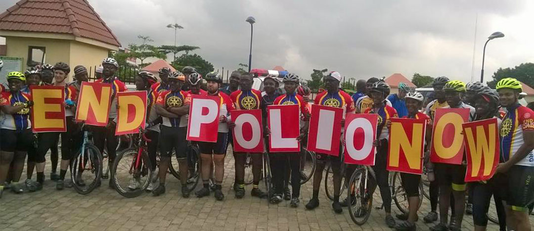 End Polio now, kuva Afriaksta. Pyöräilijät kannattelevat tekstipahveja.